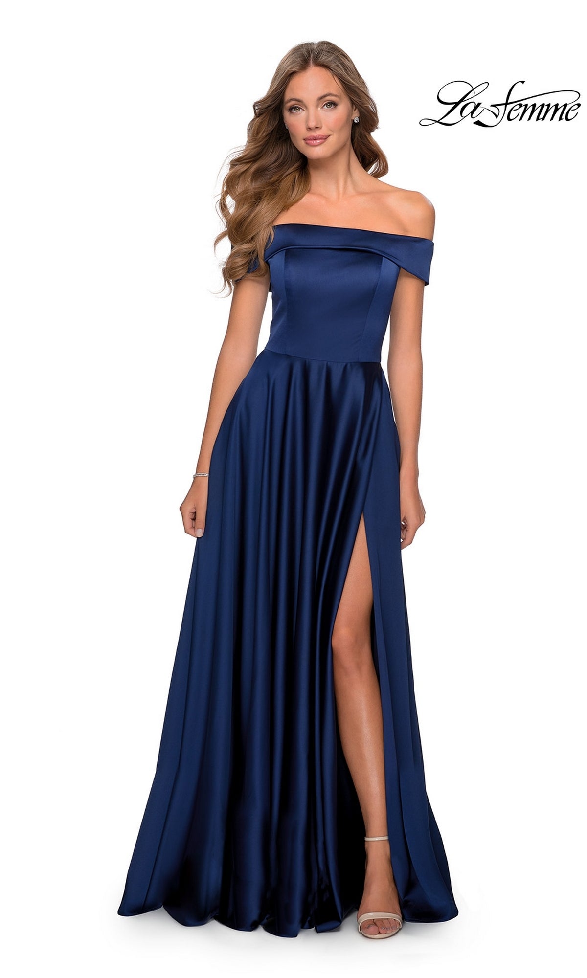 A woman poses elegantly in the La Femme Off-Shoulder Long A-Line Prom Dress 28978—a navy blue satin gown with a thigh-high slit—against a white background.